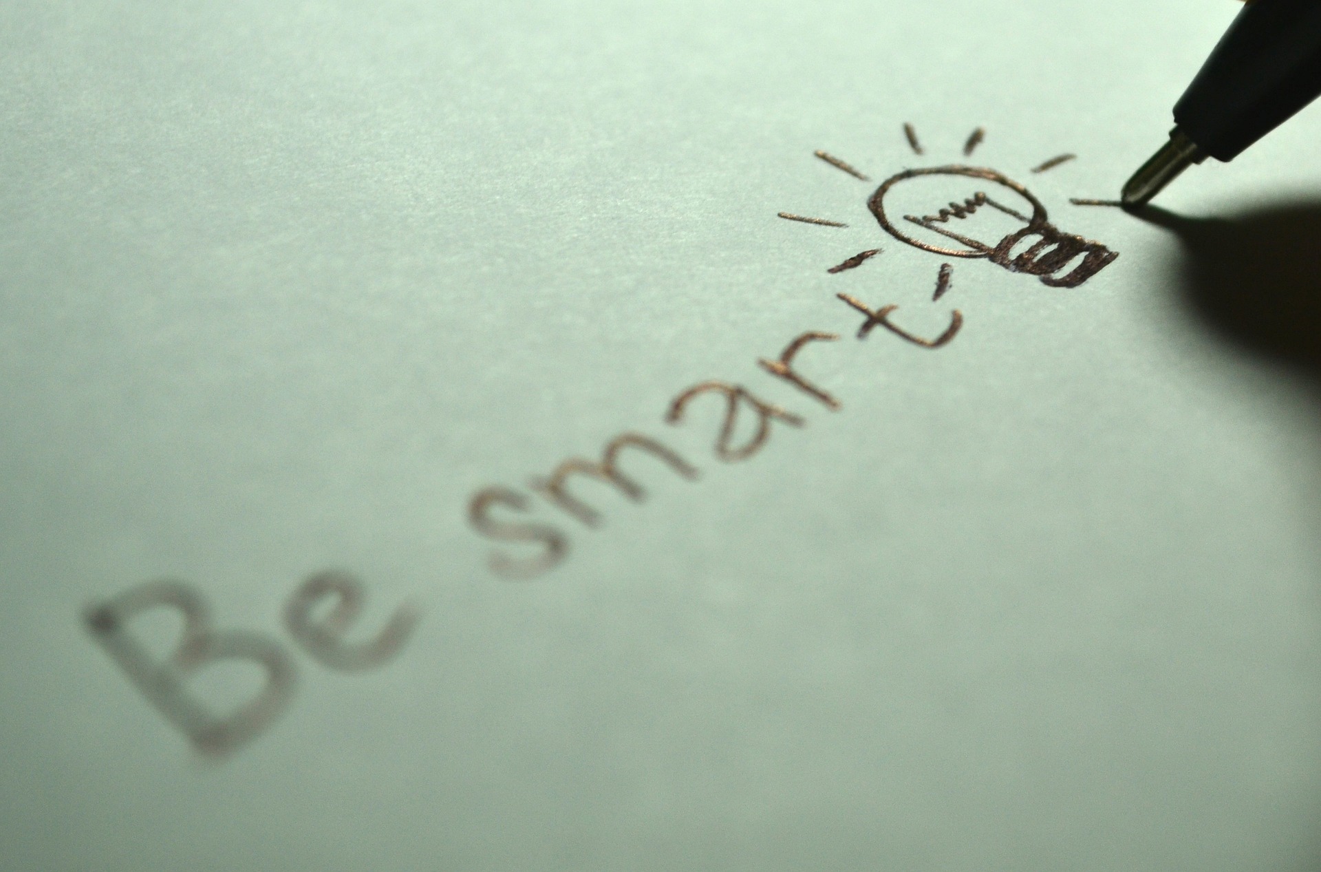 Handwritten words “Be smart” on paper, with a drawing of a light bulb next to the text, symbolizing creativity or an idea.
